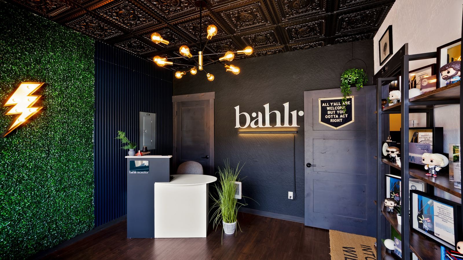 The bahlr HQ reception in Hayden: the bahlr sign lit on a black wall, a living green wall and a brass chandelier